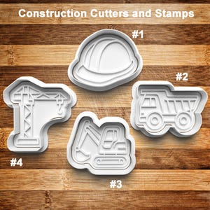 May include: White plastic construction-themed cookie cutters and stamps. The set includes a hard hat, dump truck, excavator, and crane. The text "Construction Cutters and Stamps" is at the top.