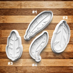 May include: Four white plastic cookie cutters shaped like feathers. The cutters are numbered 1 through 4.