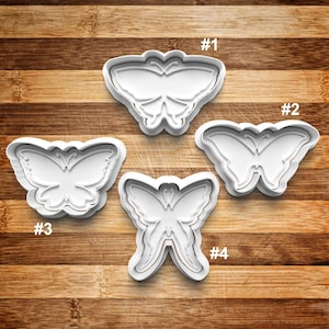May include: Four white plastic butterfly cookie cutters on a wooden surface. The cutters are numbered 1 through 4.