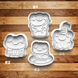May include: Four white plastic frog cookie cutters, numbered 1 through 4. The cutters are on a wooden surface.