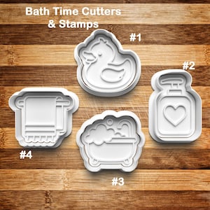 May include: White plastic cookie cutters and stamps with a bath time theme. The set includes a duck, soap dispenser with a heart, a bathtub with bubbles, and a towel on a rack. The text "Bath Time Cutters & Stamps" is at the top.
