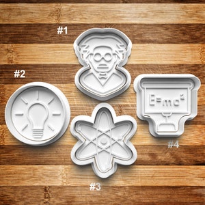 May include: Four white plastic cookie cutters shaped like a scientist, a light bulb, an atom, and a chalkboard with the equation E=mc2. The cutters are numbered 1 through 4.