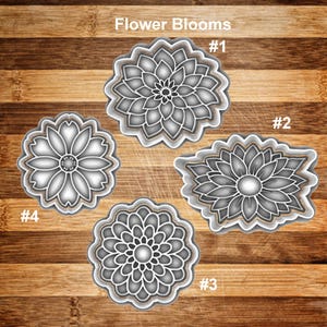 May include: Four flower-shaped cookie cutters with intricate petal designs. The cutters are in shades of gray and white, with a metallic sheen. The image includes the text "Flower Blooms" and numbers identifying each cutter.