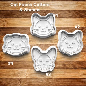May include: Four white plastic cat face cutters and stamps are displayed on a wooden surface. The cutters are numbered 1 through 4. The text "Cat Faces Cutters & Stamps" is at the top of the image.