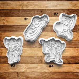 May include: Four white plastic cookie cutters shaped like angels. The cutters are numbered 1 through 4. The angels are in different poses, including playing a trumpet, holding a heart, holding an arrow, and holding a bow and arrow.