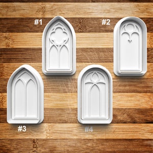 May include: Four white plastic cookie cutters shaped like different gothic arch windows. The cutters are numbered 1 through 4.