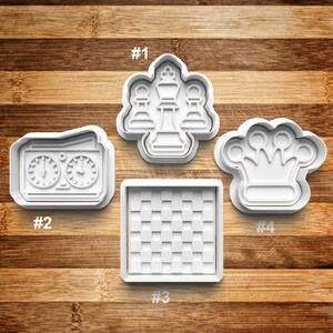 May include: Four white plastic cookie cutters shaped like chess pieces, a chessboard, and a chess clock. The cutters are numbered 1 through 4.