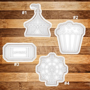 May include: Four white plastic cookie cutters shaped like a circus tent, a bucket of popcorn, an admission ticket, and a Ferris wheel. The cookie cutters are numbered 1 through 4.