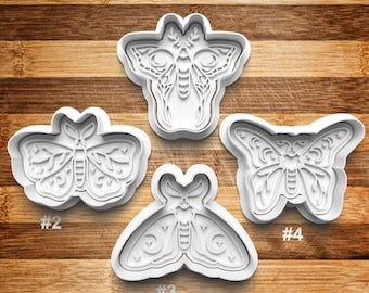 May include: Four white plastic cookie cutters shaped like moths and butterflies, labeled #1, #2, #3, and #4. Each cutter features intricate internal details including crescent moons, stars, and branch-like patterns embossed into the design.