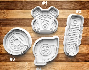 May include: Four white plastic cookie cutters shaped like car parts. The cutters are numbered 1 through 4. Cutter #1 is a car engine, #2 is a shock absorber, #3 is a brake rotor, and #4 is a turbocharger.
