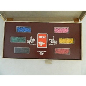 May include: An open box game of Risk, a world conquest game by Parker Brothers. The box contains a red card with the word "RISK" on it, and several small plastic pieces in different colors.