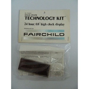 May include: A white package with a label that reads "Solid State Technology Kit" and "24 hour, 0.8" high clock display" with the Fairchild logo. The package contains a small, black circuit board.