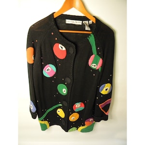 May include: Black cardigan sweater with a colorful embroidered design of billiard balls. The sweater has a button closure and is embellished with rhinestones.