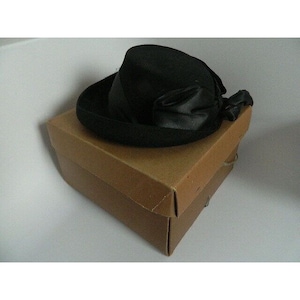 May include: A black felt hat with a wide brim and a black satin ribbon bow. The hat is in a brown cardboard box.