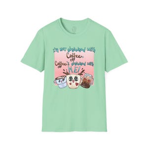 May include: A light green t-shirt with a pink and blue graphic that says "I'm not obsessed with coffee. Coffee's obsessed with me!" and features three cartoon coffee cups with faces.