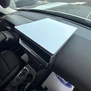 May include: A white rectangular tray cover positioned over the centre infotainment screen of a vehicle dashboard. The tray features a smooth, flat surface with a dark grey border, designed to fit securely atop the existing display unit.