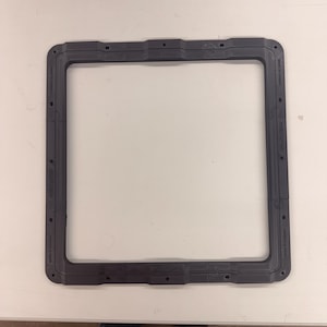 May include: A dark gray, rectangular gasket with rounded corners. The gasket has several small holes and text that reads "MADE IN CANADA". The product is designed to seal and protect.