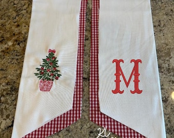 May include: White Christmas-themed banner with red gingham trim. One side features a Christmas tree embroidery in a red pot, the other a red letter "M". The text "KL Print Shop" is at the bottom.