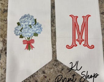 May include: Two white decorative towels. One towel features a blue hydrangea bouquet with a red bow. The other towel has a red embroidered letter "M". The text "KL Print Shop" is visible in the bottom right corner.