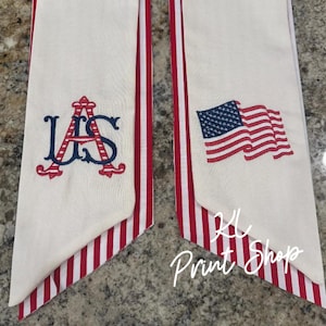 May include: Two white fabric pieces with red and white striped edges. One has a blue and red embroidered "US" monogram, the other a waving American flag. The text "KL Print Shop" is in the bottom right corner.