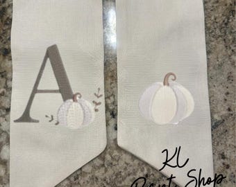 May include: Two off-white fabric banners with embroidered pumpkin designs. One banner features the letter "A" and a pumpkin, the other has a pumpkin. The text "KL Print Shop" is printed on the second banner.