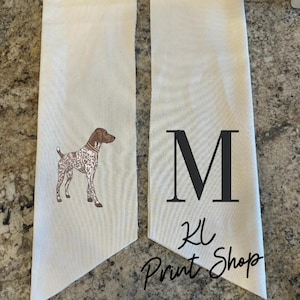 May include: Two off-white fabric banners. One banner features a brown and white dog illustration with a brown collar. The other banner has a large black letter "M", the letters "KL", and the words "Print Shop" in a script font.