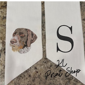 May include: Two white decorative towels. One towel features an embroidered dog head with brown and tan fur. The other towel has a large black letter "S" and the text "KL Print Shop" in black script.