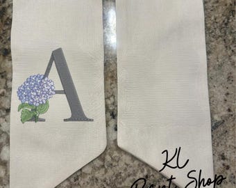 May include: A white fabric graduation sash with a gray letter A and a purple hydrangea flower design. The sash is for a graduation ceremony. The text "KL Print Shop" is visible in the bottom right corner.