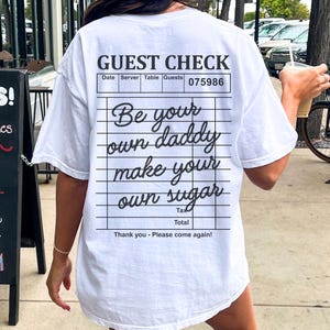 May include: White t-shirt with a black and white graphic of a guest check that says "Be your own daddy make your own sugar".