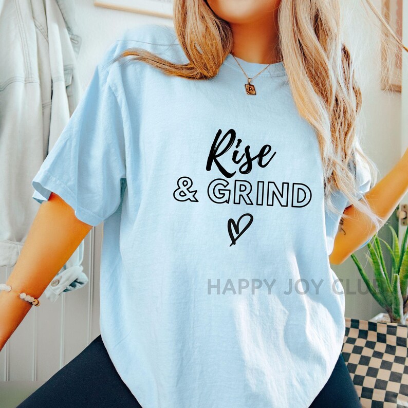 May include: A light blue t-shirt with the text "Rise & Grind" in black lettering with a heart symbol below the text.