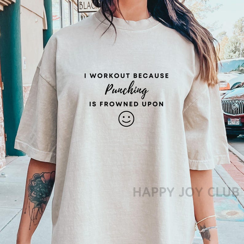May include: A light beige t-shirt with the text "I workout because punching is frowned upon" and a smiley face.