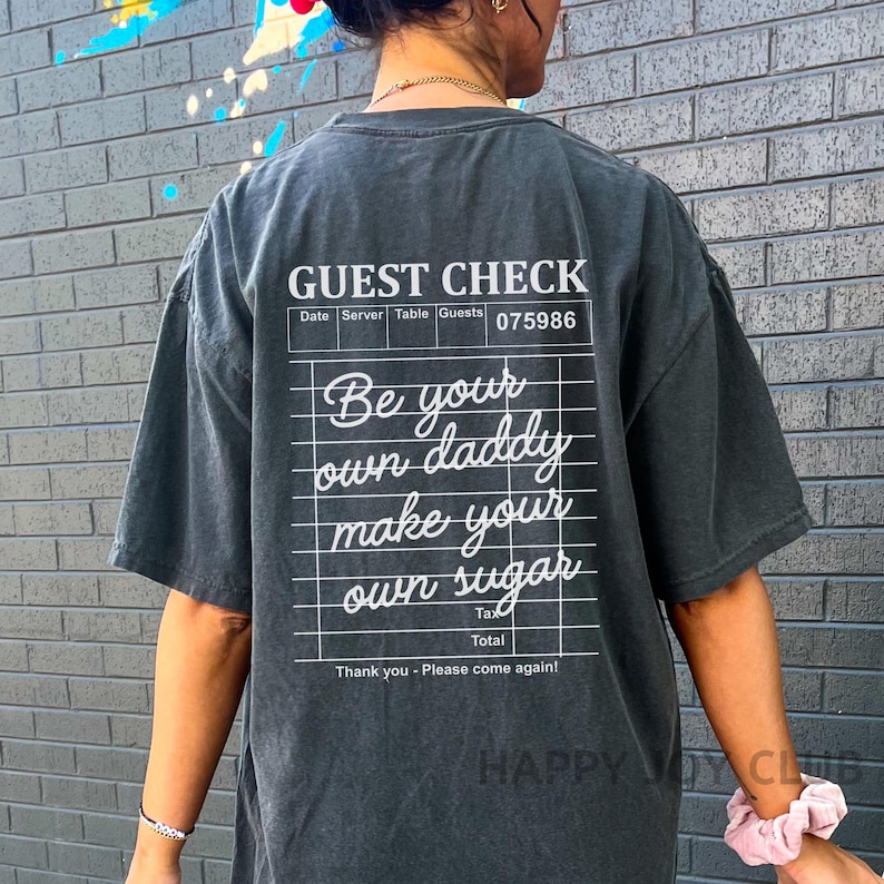Op de afbeelding: Een zwart T-shirt met een witte afbeelding van een gastenbon waarop staat "Be your own daddy make your own sugar".