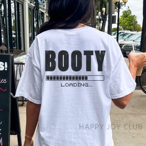 Op de afbeelding: Wit T-shirt met zwarte tekst die "BOOTY LOADING..." luidt, met een voortgangsbalk eronder.