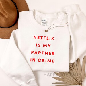 May include: White sweatshirt with red text that reads "Netflix is my partner in crime".
