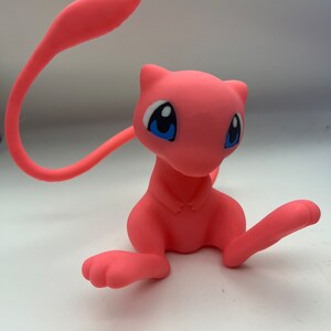 May include: A pink and white Pokemon figurine of a sitting Mewtwo with blue eyes.
