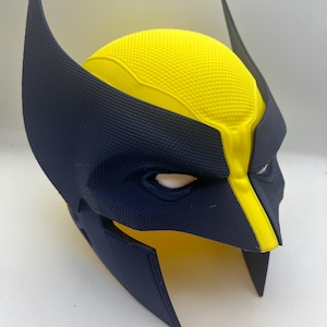 May include: A yellow and blue plastic mask with a textured surface. The mask has a pointed top and a wide, flat bottom. The mask is designed to resemble a superhero's helmet.