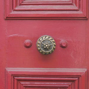 Może przedstawiać: Zbliżenie czerwonych drewnianych drzwi z mosiężnym klamką. Klamka ma kształt gwiazdy.