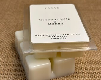 May include: A set of wax melts in a clear plastic container. The wax melts are white and have a label that reads "VASAR Coconut Milk & Mango HANDPOURED IN VENICE CA WAX MELTS 2.50 oz | 70 g".