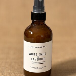 May include: A brown glass bottle with a black spray nozzle and a white label that reads "YASAK CANDLE CO. WHITE SAGE & LAVENDER ROOM & LINEN SPRAY POURED IN VENICE CA 4 fl oz | 118 ml".