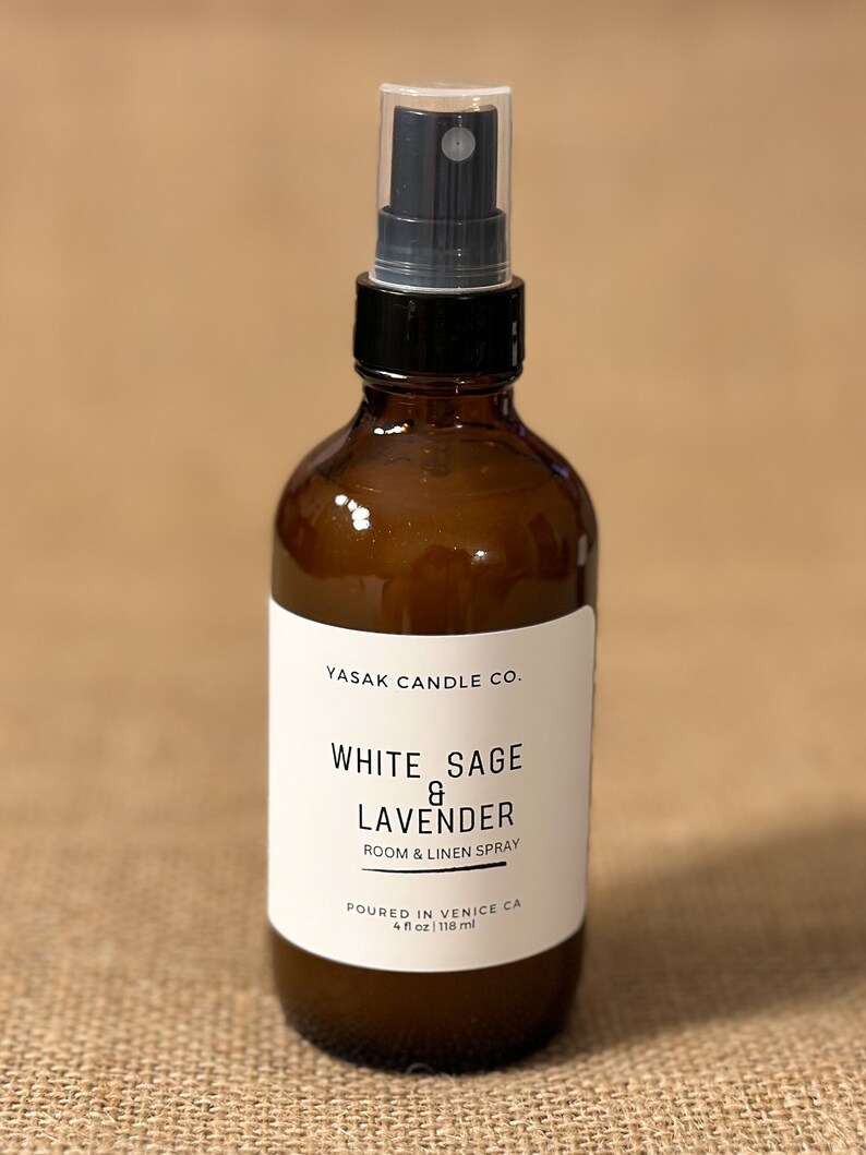 May include: A brown glass bottle with a black spray nozzle and a white label that reads "YASAK CANDLE CO. WHITE SAGE & LAVENDER ROOM & LINEN SPRAY POURED IN VENICE CA 4 fl oz | 118 ml".