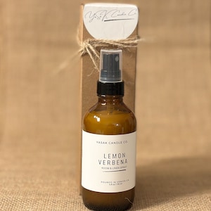 以下が含まれることがあります： 黒いスプレーノズルが付いた茶色のガラス瓶。瓶には「YASAK CANDLE CO. LEMON VERBENA ROOM & LINEN SPRAY POURED IN VENICE CA 4 fl oz / 118 ml」とラベルが貼られています。