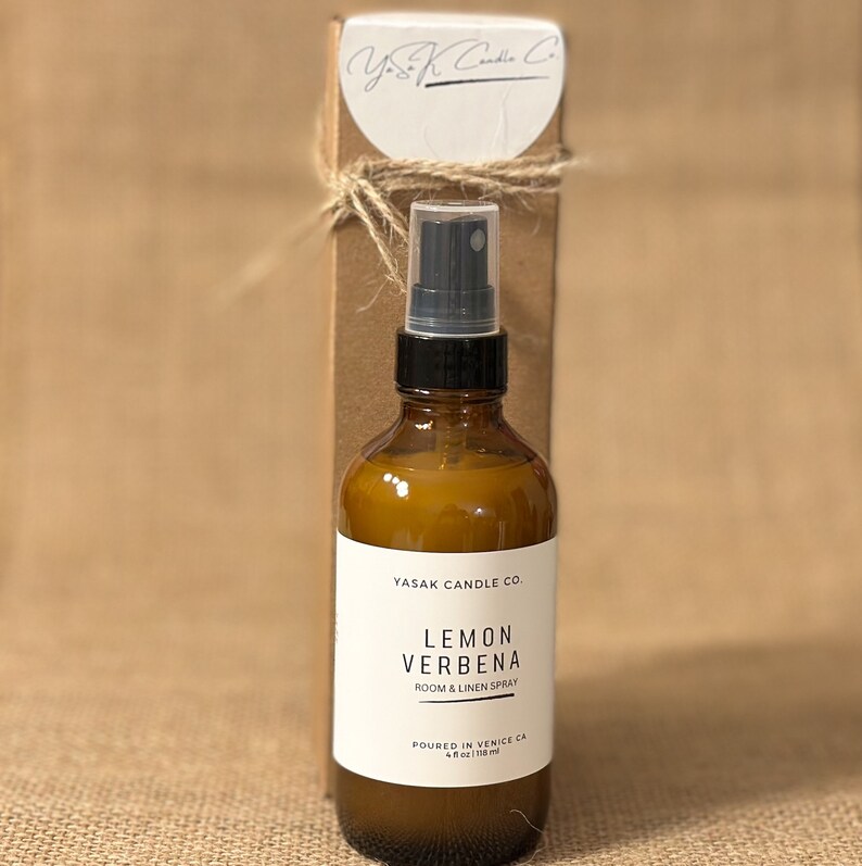 以下が含まれることがあります： 黒いスプレーノズルが付いた茶色のガラス瓶。瓶には「YASAK CANDLE CO. LEMON VERBENA ROOM & LINEN SPRAY POURED IN VENICE CA 4 fl oz / 118 ml」とラベルが貼られています。