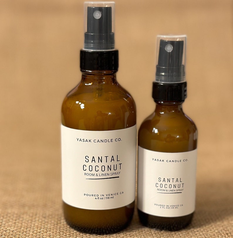 May include: Two amber glass bottles with black spray tops. The bottles are labeled "YASAK CANDLE CO." and "SANTAL COCONUT ROOM & LINEN SPRAY". The larger bottle is 4 fl oz / 118 ml and the smaller bottle is 2 fl oz / 59 ml.