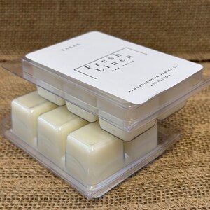 May include: A clear plastic clamshell package containing six wax melts. The top label reads "Fresh Linen Wax Melts" and "Handpoured in Venice CA 2.50 oz 70 g". The wax melts are a creamy off-white color.