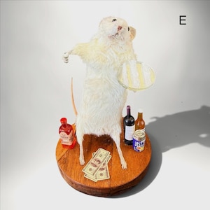 May include: A taxidermy white rat standing on a circular wooden base, holding a small round tray. The display includes miniature bottles of red and amber liquid, a small blue can with Japanese text, and several miniature one-hundred dollar bills.