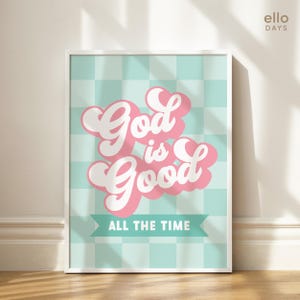 May include: A white framed print with a light blue and white checkered background. The text "God is Good" is in pink with a white outline and a banner below that reads "All the Time".