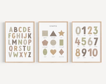 May include: Three framed prints with educational content for children. The first print features the alphabet in brown, green, and pink letters. The second print shows various shapes with their names: square, triangle, star, pentagon, circle, rectangle, oval, heart, and diamond. The third print shows the numbers 0-10 in brown, green, and pink with the words zero, one, two, three, four, five, six, seven, eight, nine, and ten written below each number.