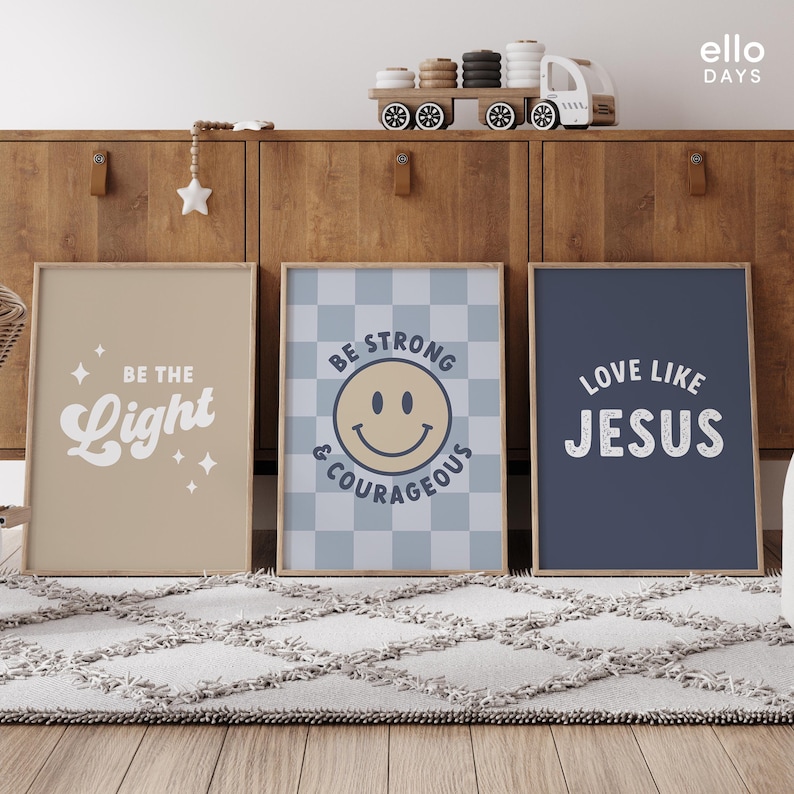 May include: Three framed prints with inspirational messages. The first print is beige with the text "Be the Light" in a retro font. The second print is blue and white checkered with the text "Be Strong & Courageous" and a yellow smiley face. The third print is navy blue with the text "Love Like Jesus" in a white distressed font.