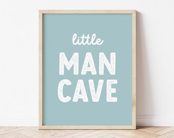 May include: A framed print with the words "little MAN CAVE" in white, block letters on a light blue background. The frame is a light wood color. The word "ello DAYS" is printed in the bottom left corner.