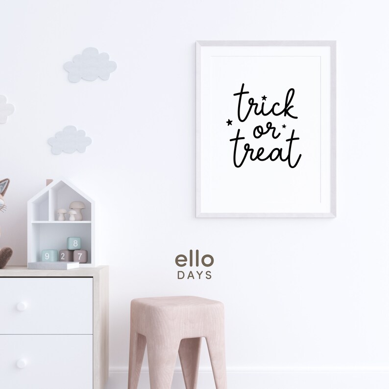 May include: White framed print with black text that reads "trick or treat" with stars on either side of "or". The print is hanging on a white wall with a white dresser and a pink stool in the foreground.